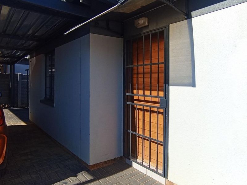 Front entrance area featuring a timber door with a security gate, adjacent to a covered carport with paved driveway.
