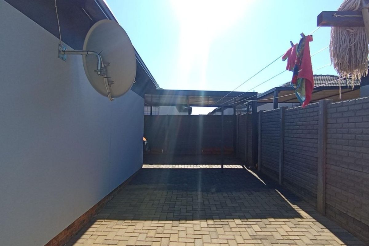 A paved rear exterior area featuring a precast concrete boundary wall, a mounted satellite dish, and a functional washing line.