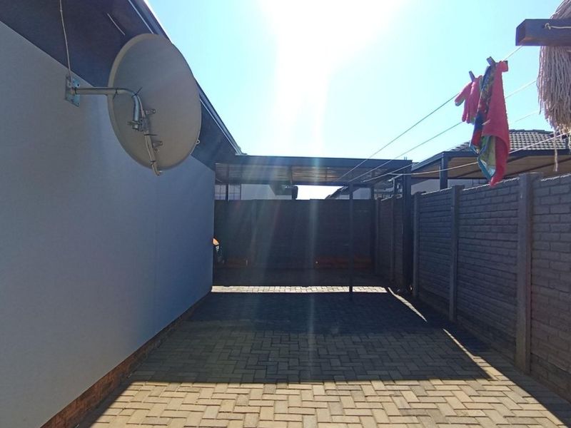 A paved rear exterior area featuring a precast concrete boundary wall, a mounted satellite dish, and a functional washing line.