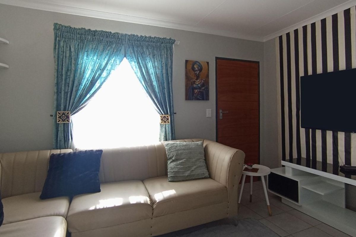 A living room featuring tiled flooring, cove cornicing, and a timber door, with a feature wall behind the television area.
