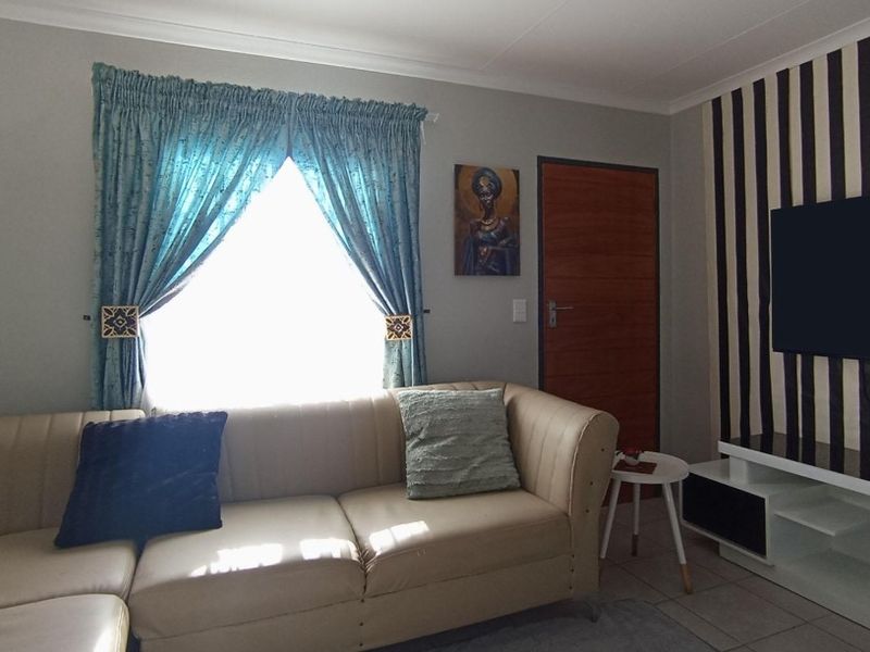 A living room featuring tiled flooring, cove cornicing, and a timber door, with a feature wall behind the television area.