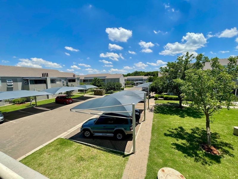 An elevated view of the townhouse complex parking area featuring shade cloth carports, paved driveways, and well-maintained communal garden spaces.