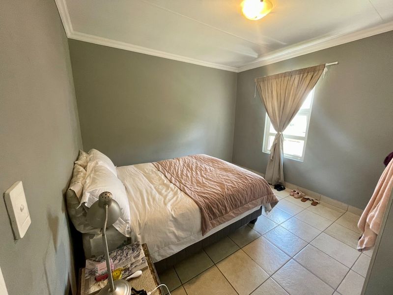 A functional bedroom featuring tiled flooring, neutral wall tones, and a window with curtain fixtures, providing a clean and simple living space.