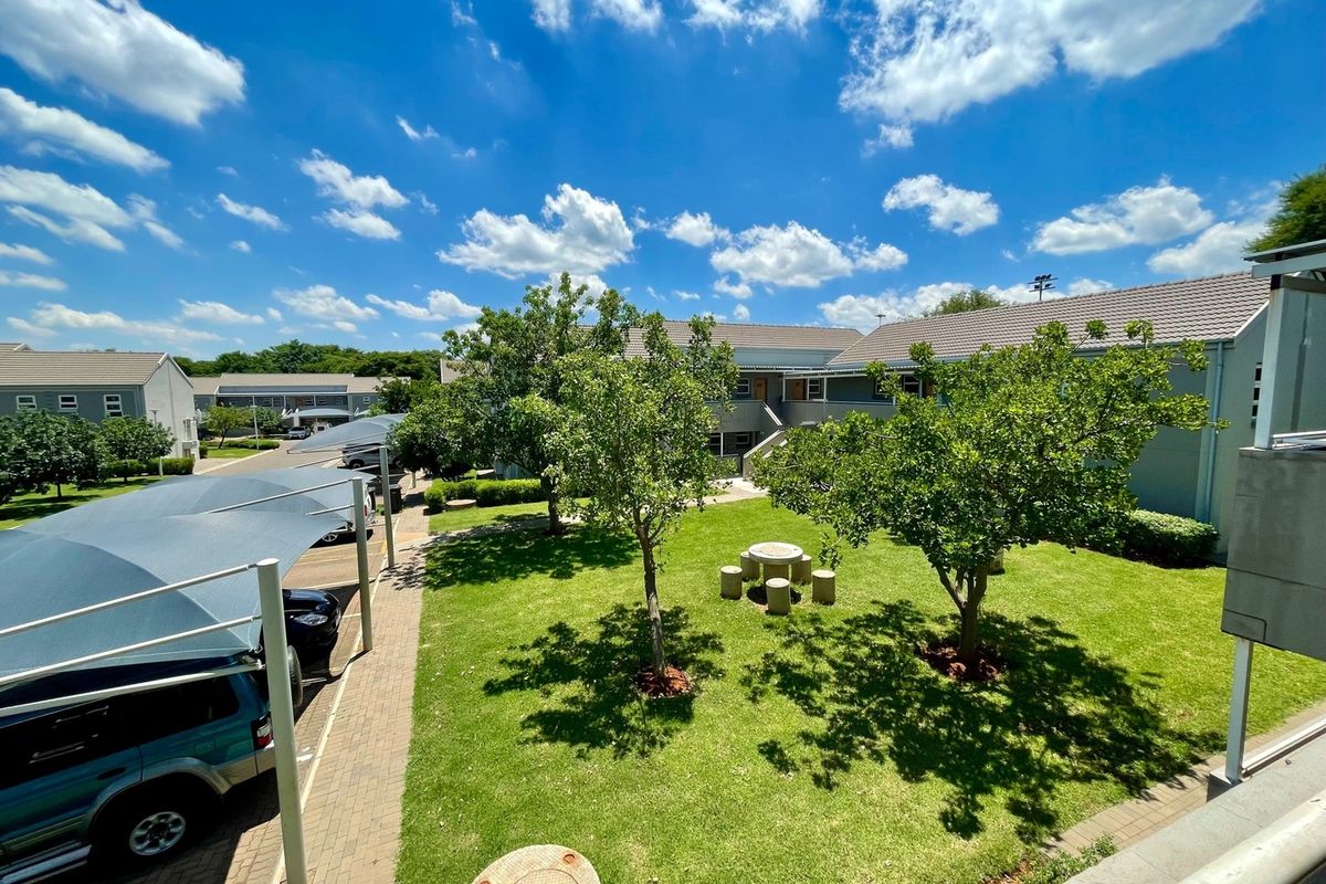 Elevated view of a well-maintained communal garden area featuring mature trees, paved walkways, and covered parking bays within the townhouse complex.