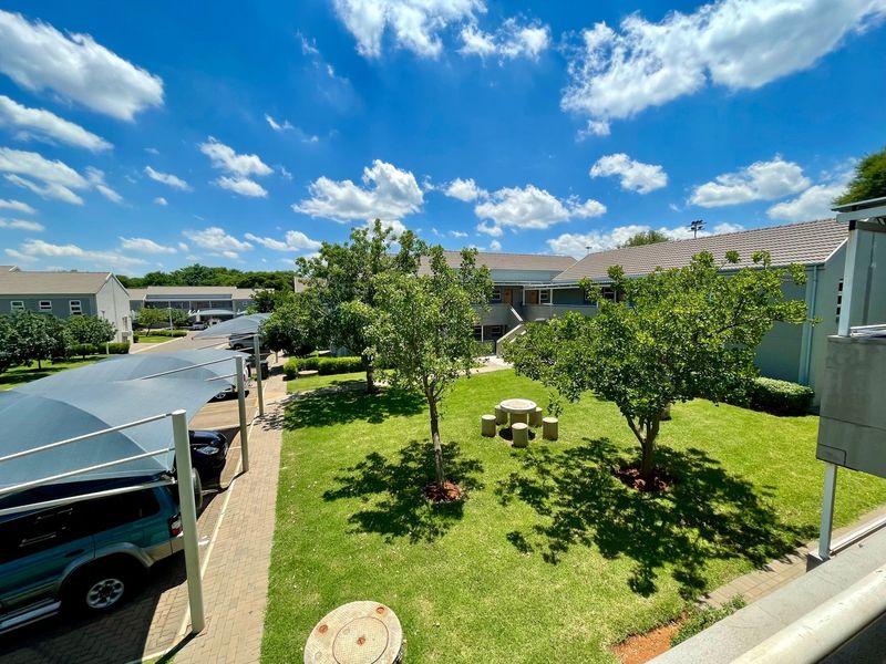 Elevated view of a well-maintained communal garden area featuring mature trees, paved walkways, and covered parking bays within the townhouse complex.