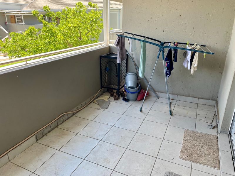 A covered balcony area featuring tiled flooring and a metal balustrade, currently used as a utility space.