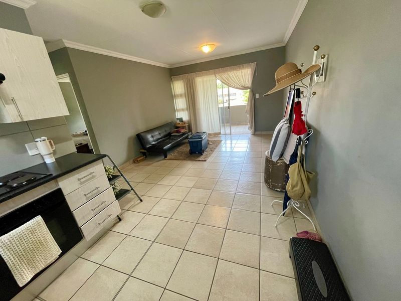 Open-plan living area featuring tiled flooring, a compact kitchen with built-in cabinetry, and direct access to a balcony through sliding glass doors.