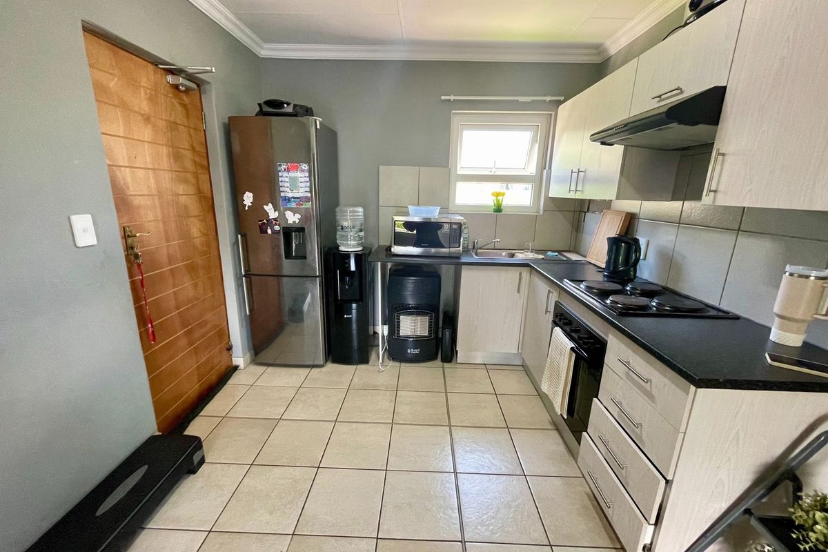 A functional kitchen featuring light-toned cabinetry, dark countertops, tiled flooring, and integrated appliances including an oven, hob, and extractor fan.