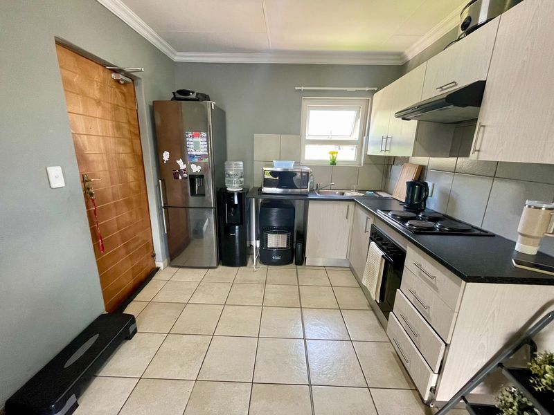 A functional kitchen featuring light-toned cabinetry, dark countertops, tiled flooring, and integrated appliances including an oven, hob, and extractor fan.