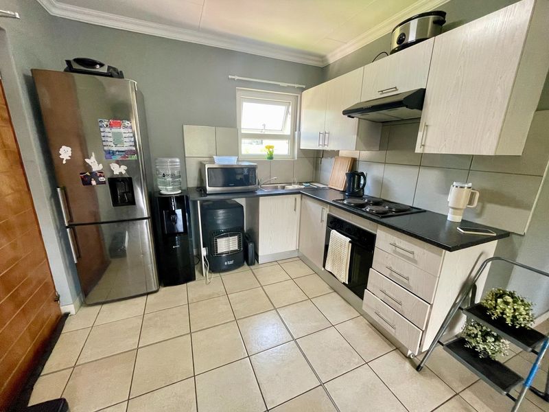 Functional kitchen featuring light wood-finish cabinetry, dark countertops, built-in oven and hob, tiled backsplash, and tiled flooring.