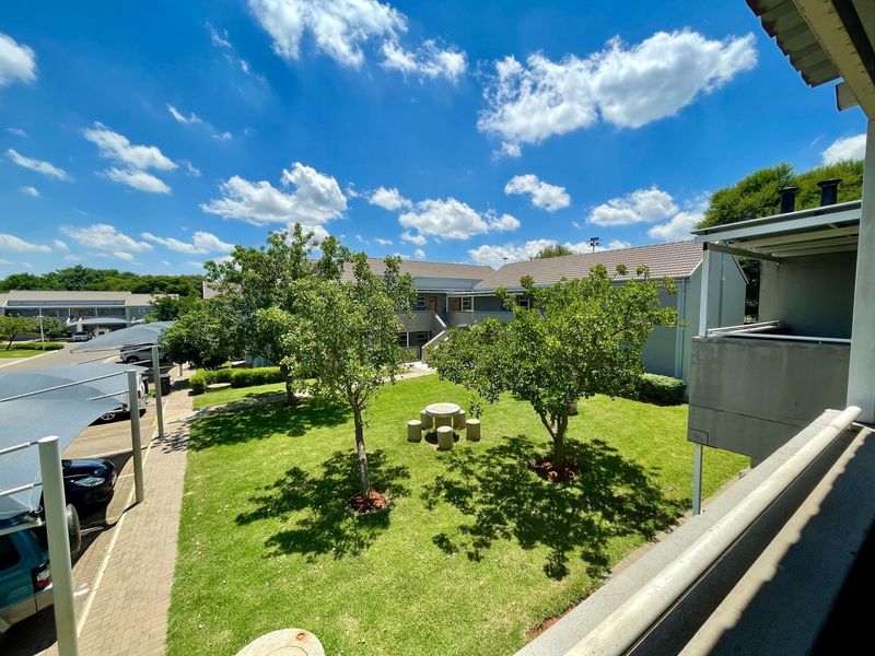 Elevated view overlooking a well-maintained communal garden area with mature trees and adjacent paved parking with shade cloth carports.