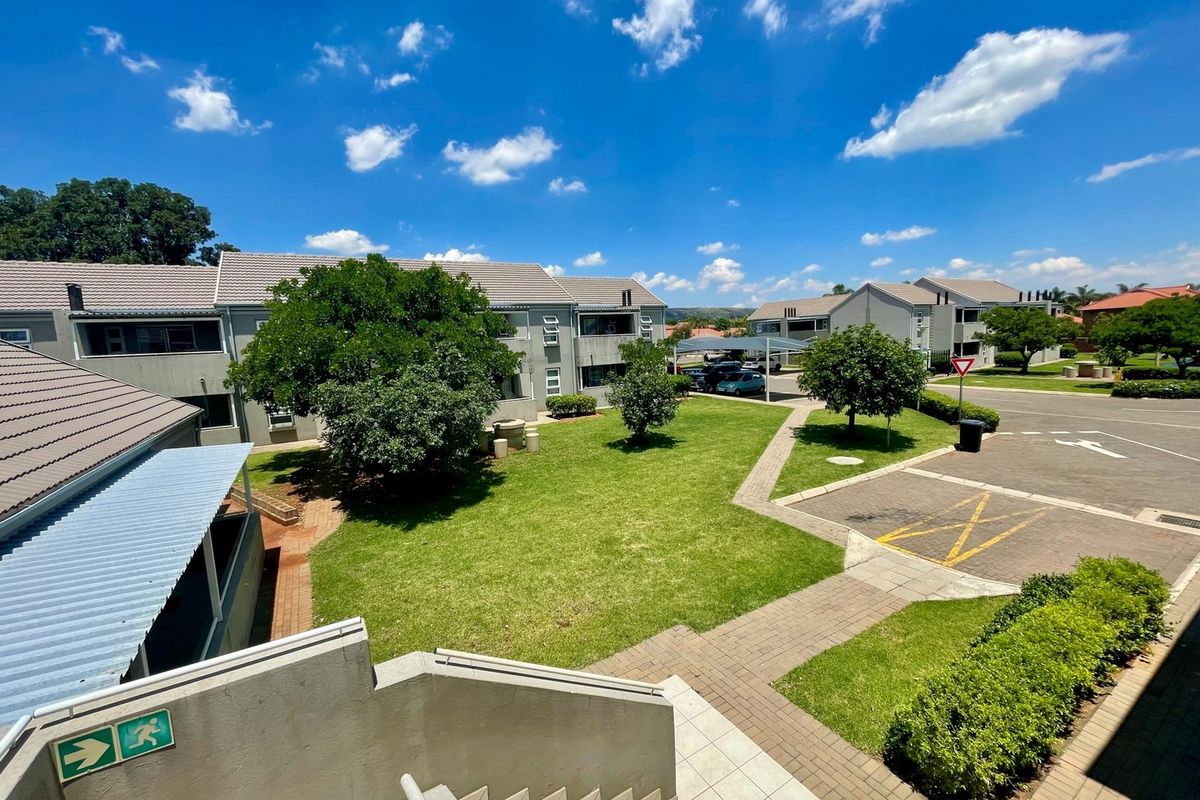 An elevated view of the townhouse complex grounds, featuring well-maintained lawns, paved pathways, and covered parking areas under a clear blue sky.