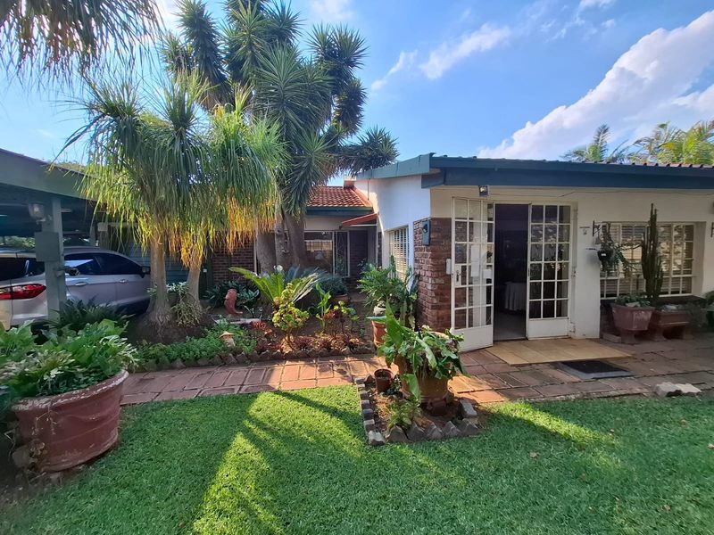 A rear exterior view of the house featuring a brick facade, french doors leading to a patio, and an established garden with a carport.