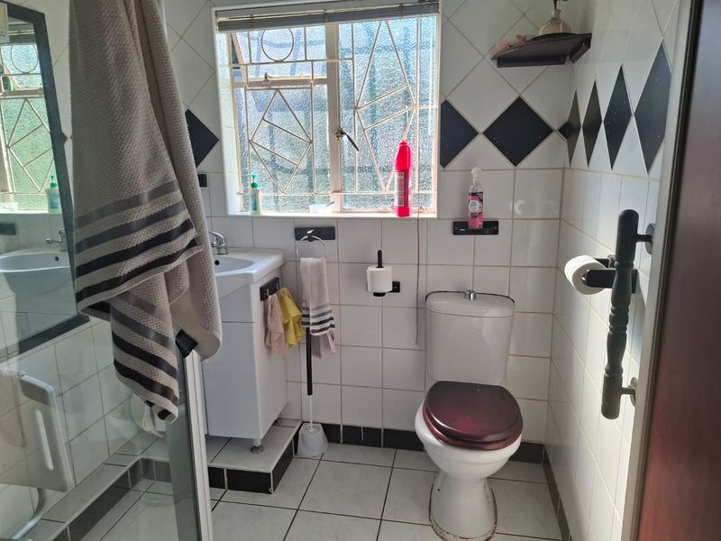 A compact bathroom featuring a shower enclosure, pedestal basin, and toilet, finished with classic white and black tiled walls and flooring.