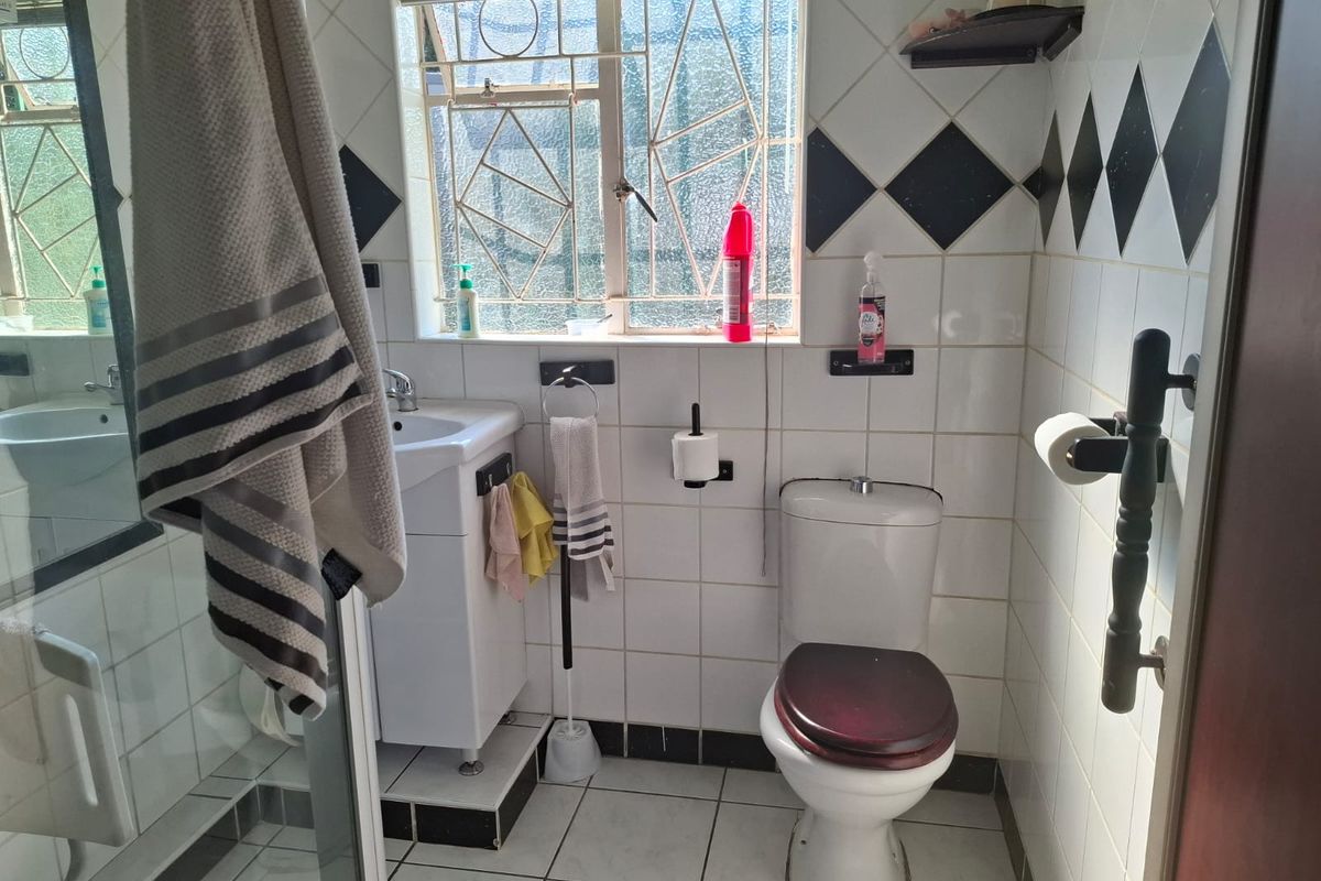 A compact bathroom featuring a shower enclosure, pedestal basin, and toilet, finished with classic white and black tiled walls and flooring.