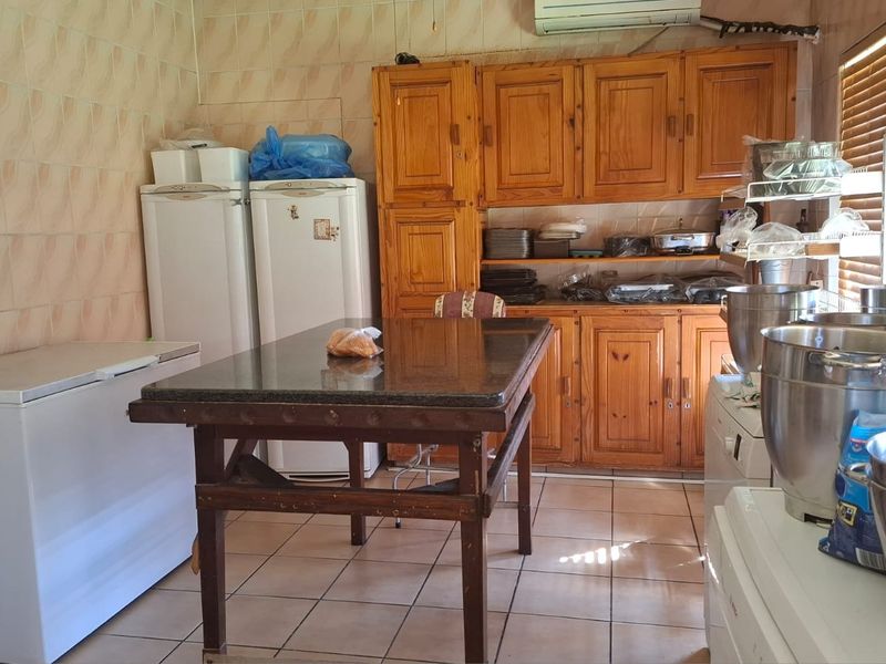 A functional kitchen space featuring wooden cabinetry, granite countertops, and tiled finishes, currently utilized as a commercial-style food preparation area.