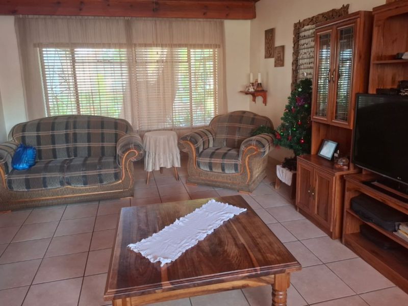 A comfortable living room featuring ceramic floor tiles, exposed timber ceiling beams, and large windows fitted with venetian blinds.