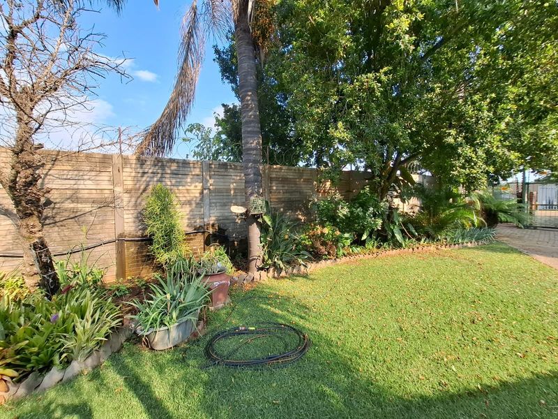A private garden area featuring a well-established lawn, mature trees, and a secure boundary wall with razor wire fencing.