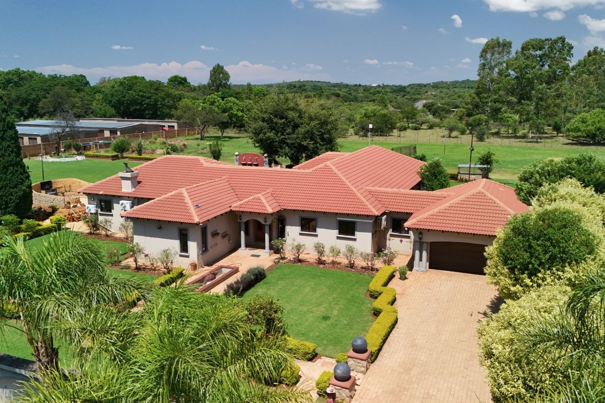 Aerial view of a spacious single-story residential property featuring a terracotta tile roof, paved driveway, double garage, and well-maintained landscaped gardens.
