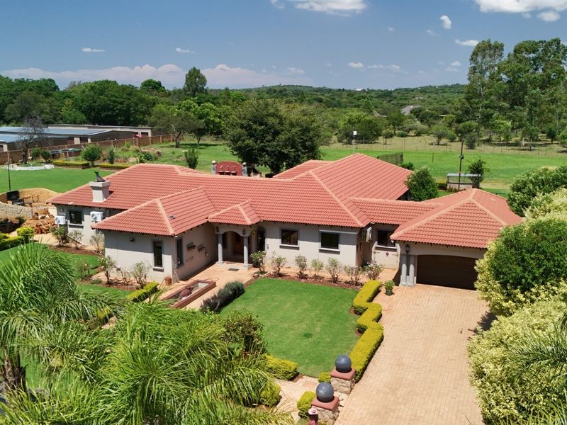 Aerial view of a spacious single-story residential property featuring a terracotta tile roof, paved driveway, double garage, and well-maintained landscaped gardens.