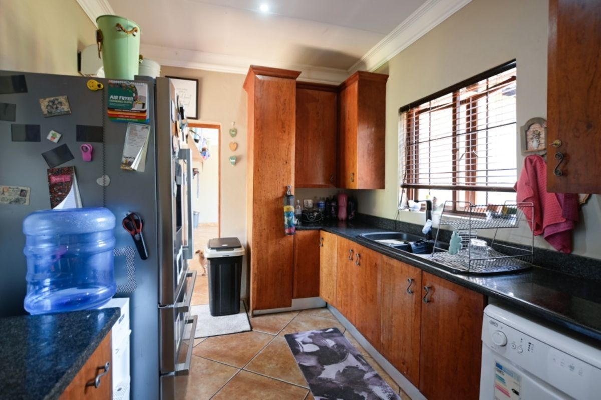 A functional kitchen featuring wooden cabinetry, granite countertops, tiled flooring, and a window with venetian blinds.