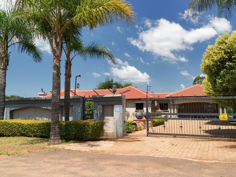 Front view of a residential property featuring a secure gated entrance, paved driveway, perimeter wall with electric fencing, and a tiled roof structure.