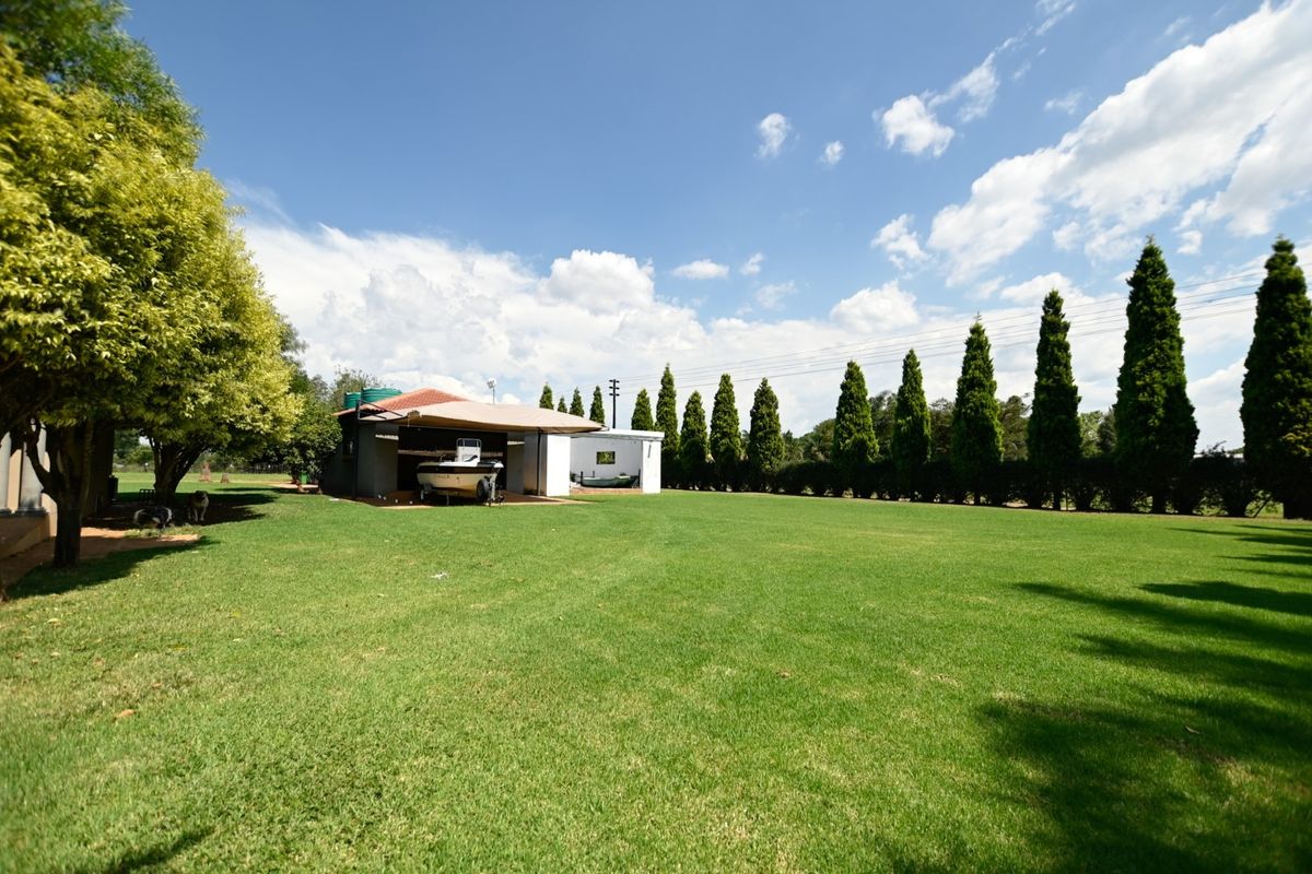 Spacious rear garden featuring a well-maintained lawn, mature trees, and a covered outdoor structure with adjacent outbuilding.