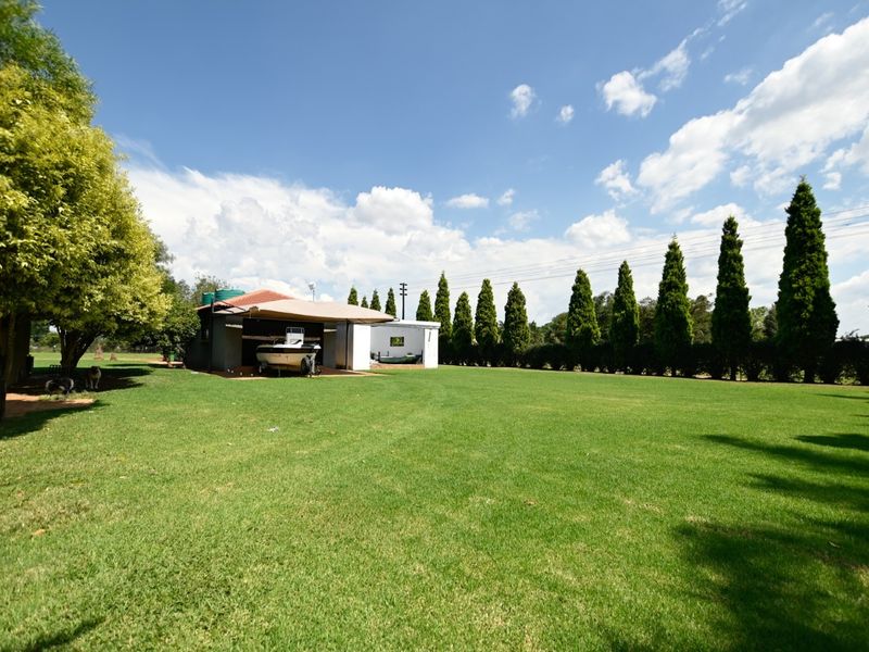 Spacious rear garden featuring a well-maintained lawn, mature trees, and a covered outdoor structure with adjacent outbuilding.