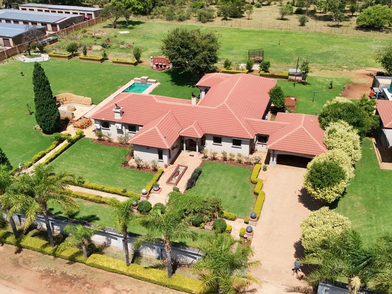 Aerial view of a spacious residential property featuring a large landscaped garden, swimming pool, tiled roof house, and a paved driveway with carport.