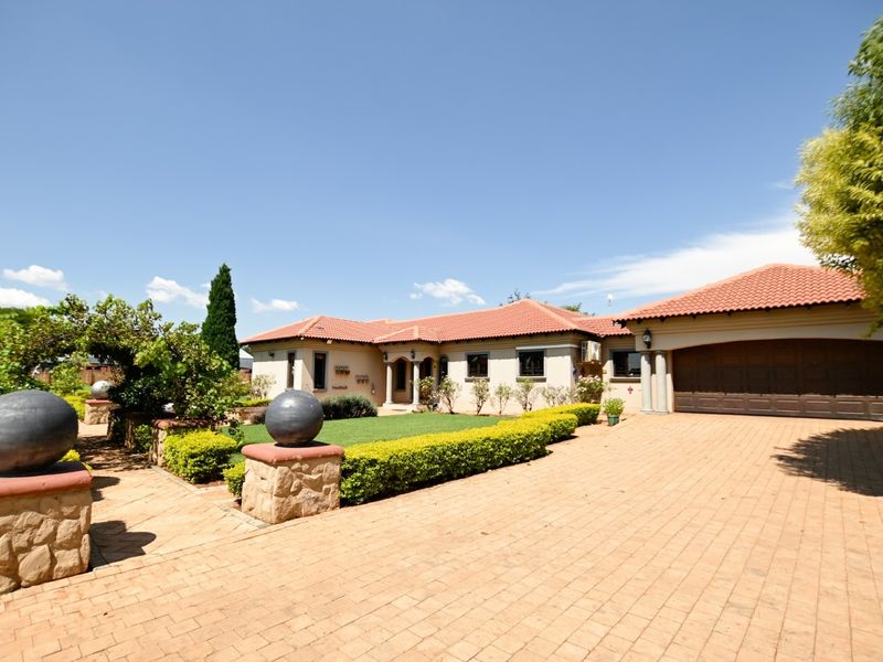 A well-maintained front elevation featuring a paved driveway, double garage, tiled roof, and landscaped garden with stone-clad architectural details.
