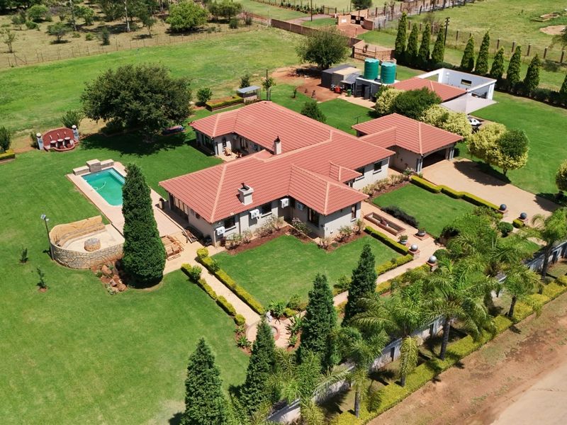 Aerial view of a spacious residential property featuring a large landscaped garden, swimming pool, tiled roof house, and detached garage structure.