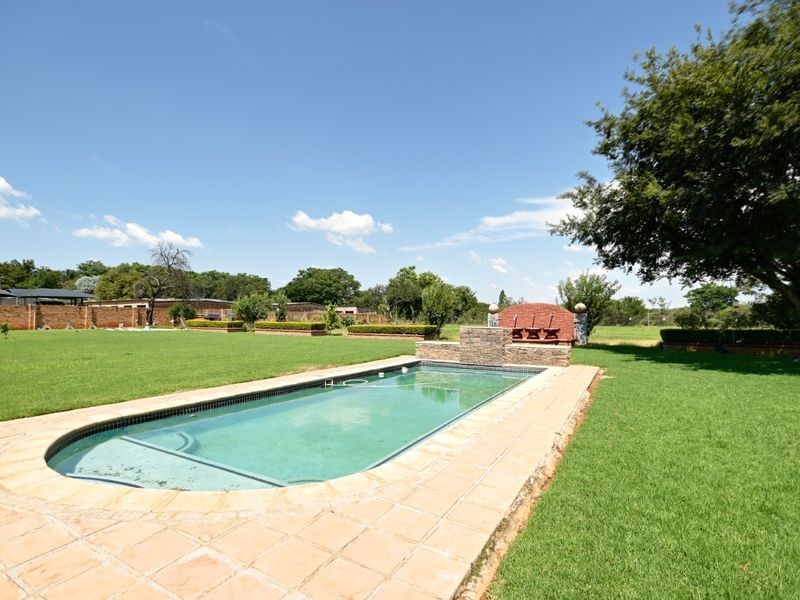Spacious outdoor area featuring a swimming pool with a stone water feature, brick braai, and expansive lawn, ideal for outdoor entertaining.