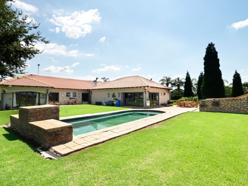 Spacious rear garden featuring a swimming pool, stone-clad retaining wall, paved patio area, and well-maintained lawn, perfect for outdoor entertaining.