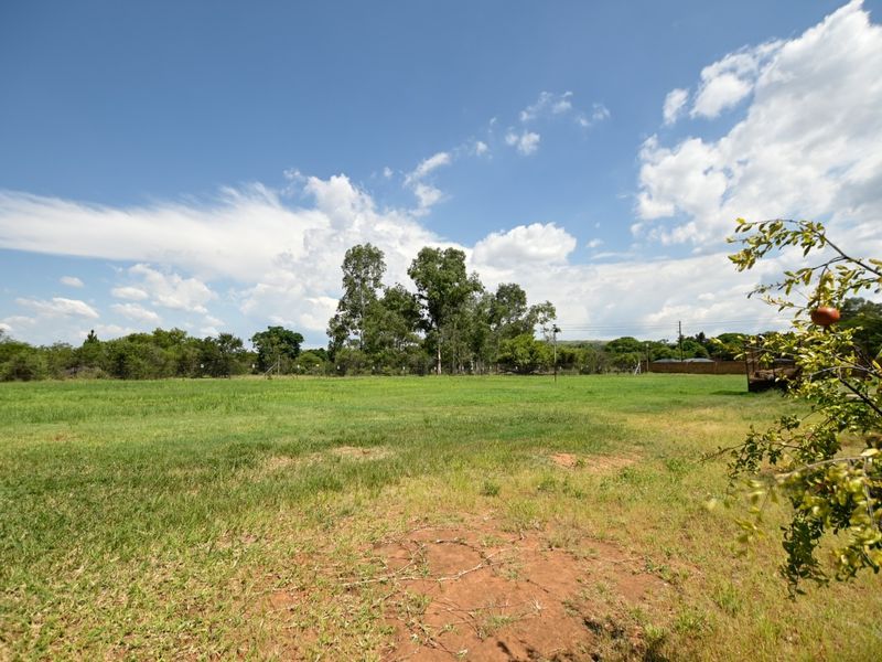 A wide, open grassy plot featuring mature trees and perimeter fencing, offering a spacious outdoor area with natural landscaping.
