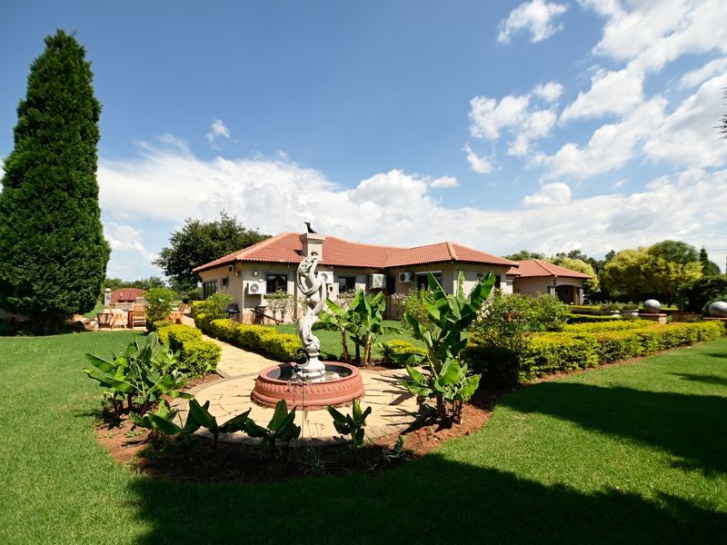 A well-maintained rear garden featuring a central stone fountain, paved pathways, manicured hedges, and a view of the tiled-roof house exterior.