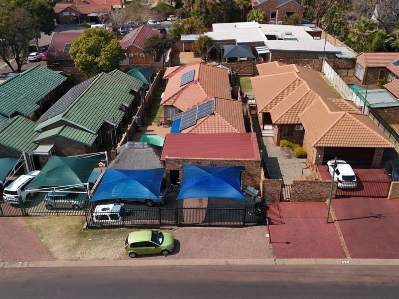 Aerial view of a residential complex featuring multiple houses with tiled roofs, solar panels, paved driveways, and outdoor shade structures.