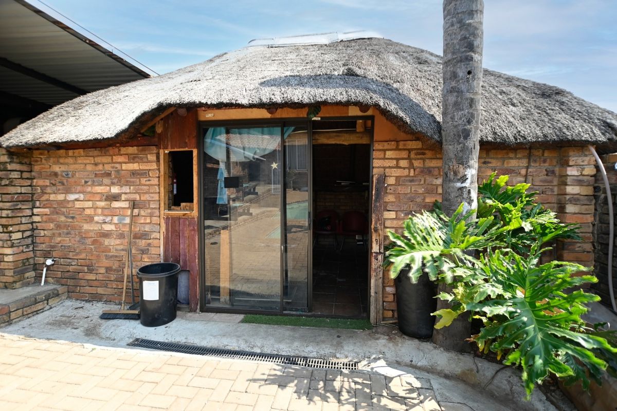 A rustic outdoor entertainment area featuring a traditional thatch roof, exposed brick construction, and a sliding glass door leading to the interior space.