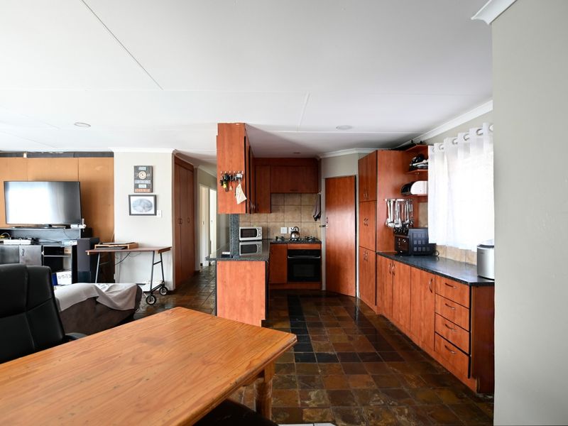 Open-plan kitchen and living area featuring wooden cabinetry, granite countertops, built-in oven, gas hob, and tiled flooring throughout.