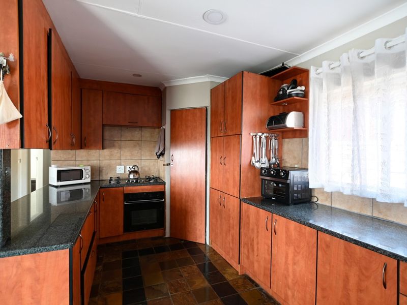 A functional kitchen featuring wood-look laminate cabinetry, granite countertops, a built-in oven with gas hob, and durable slate floor tiles.