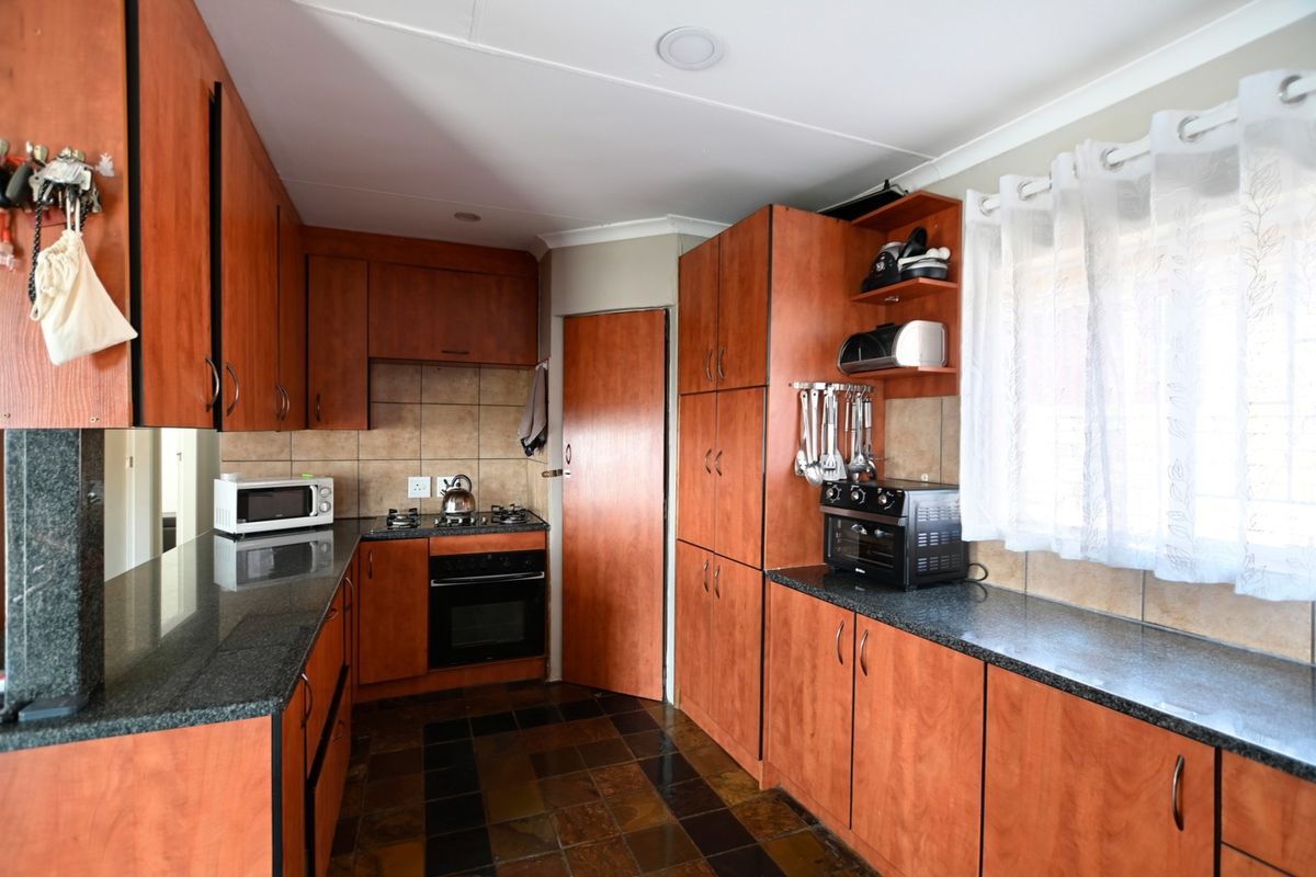 A functional kitchen featuring wood-look laminate cabinetry, granite countertops, a built-in oven with gas hob, and durable slate floor tiles.
