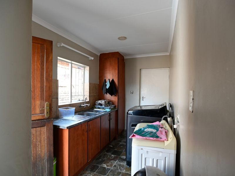 A functional laundry room featuring built-in wooden cabinetry, a stainless steel sink, and tiled flooring with direct access to the exterior.