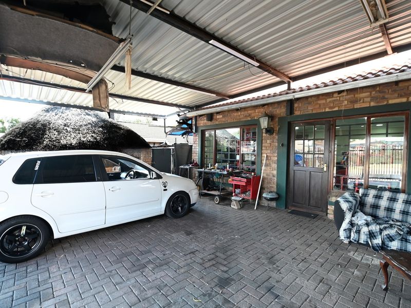 A covered outdoor parking area or garage featuring a corrugated metal roof, brick exterior walls, and paved flooring.