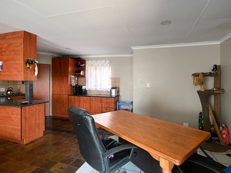 Open plan kitchen and dining area featuring wooden cabinetry, granite countertops, gas hob, and tiled flooring with a visible ceiling water stain.