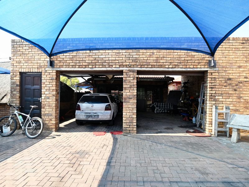 A double garage featuring a face brick exterior and a protective blue shade cloth canopy over the paved driveway area.