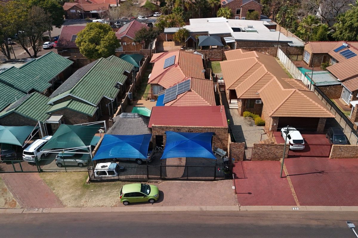 Aerial view of a residential complex featuring multiple houses with tiled roofs, solar panels, paved driveways, and outdoor shade structures.
