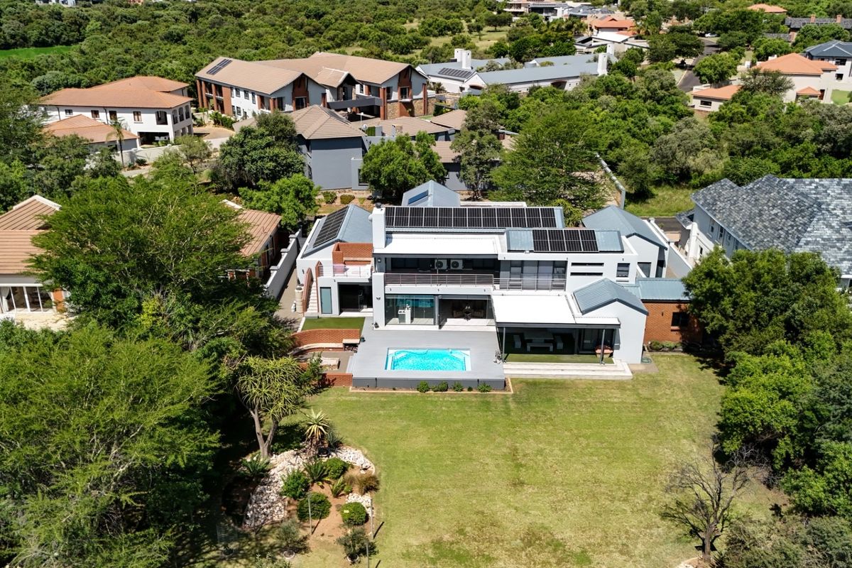 Aerial view of a modern multi-story residence featuring solar panels, a swimming pool, a spacious patio, and a well-maintained garden.
