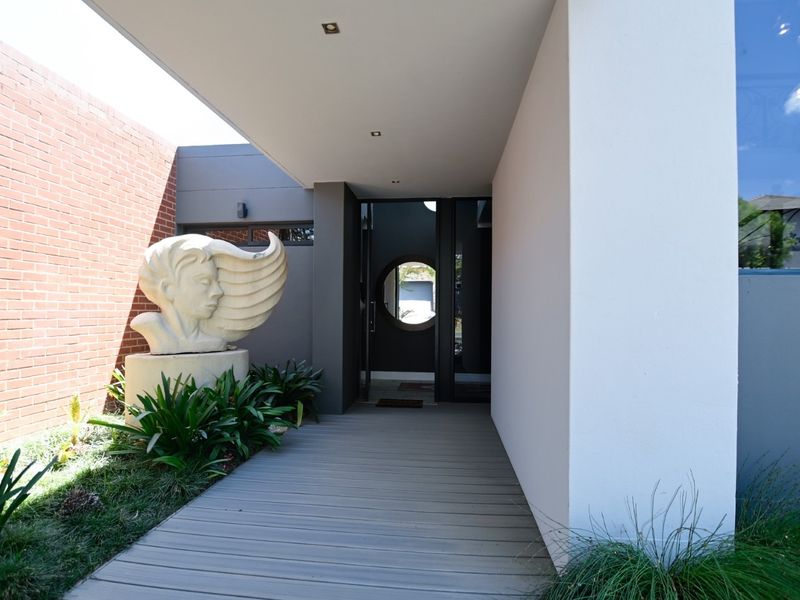 A modern, well-maintained entrance featuring a timber deck walkway, brick feature wall, and a distinctive circular window design.