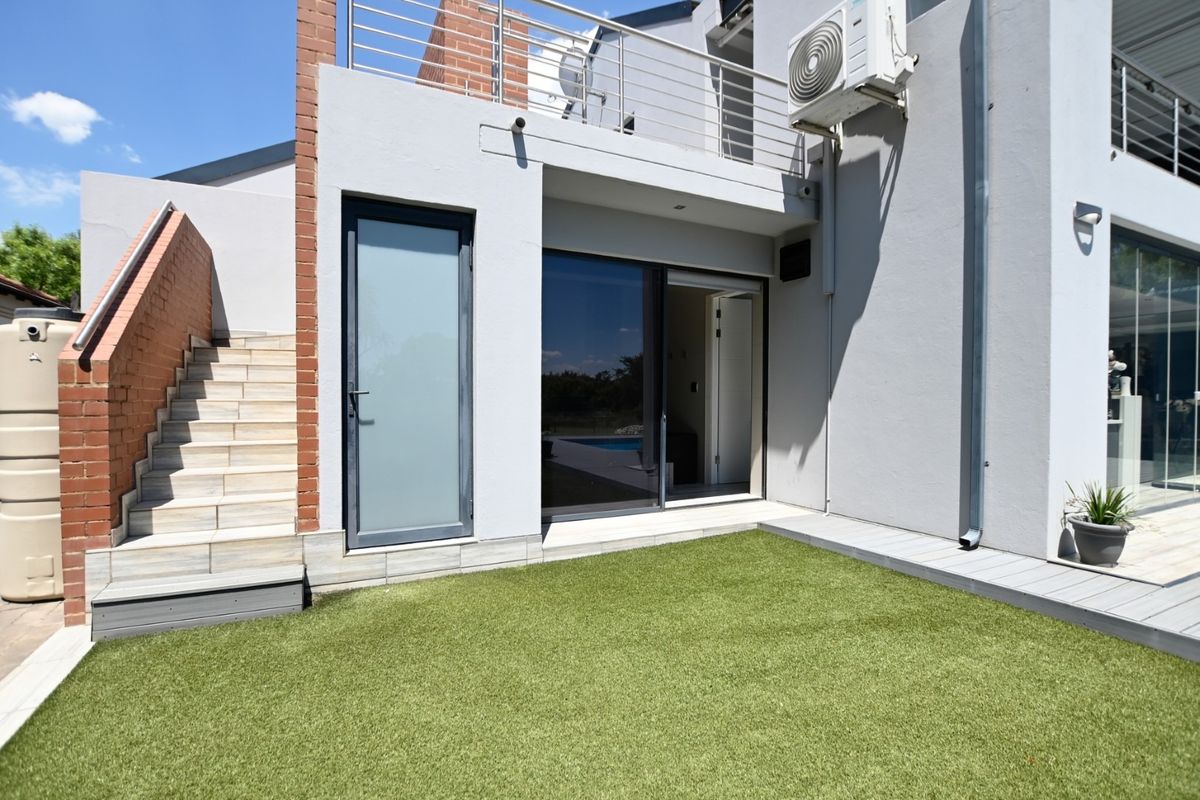 Rear exterior view featuring a small artificial lawn, tiled staircase with brick accents, and a balcony with stainless steel balustrades.
