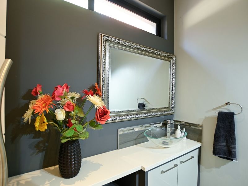 Modern bathroom vanity featuring a glass vessel sink, stone countertop, and sleek cabinetry, accented by a dark feature wall and clerestory window.