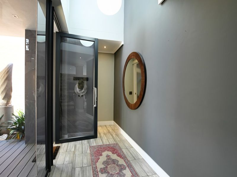 Modern entrance foyer featuring a large glass pivot door, double volume ceiling, recessed lighting, and contemporary tiled flooring.